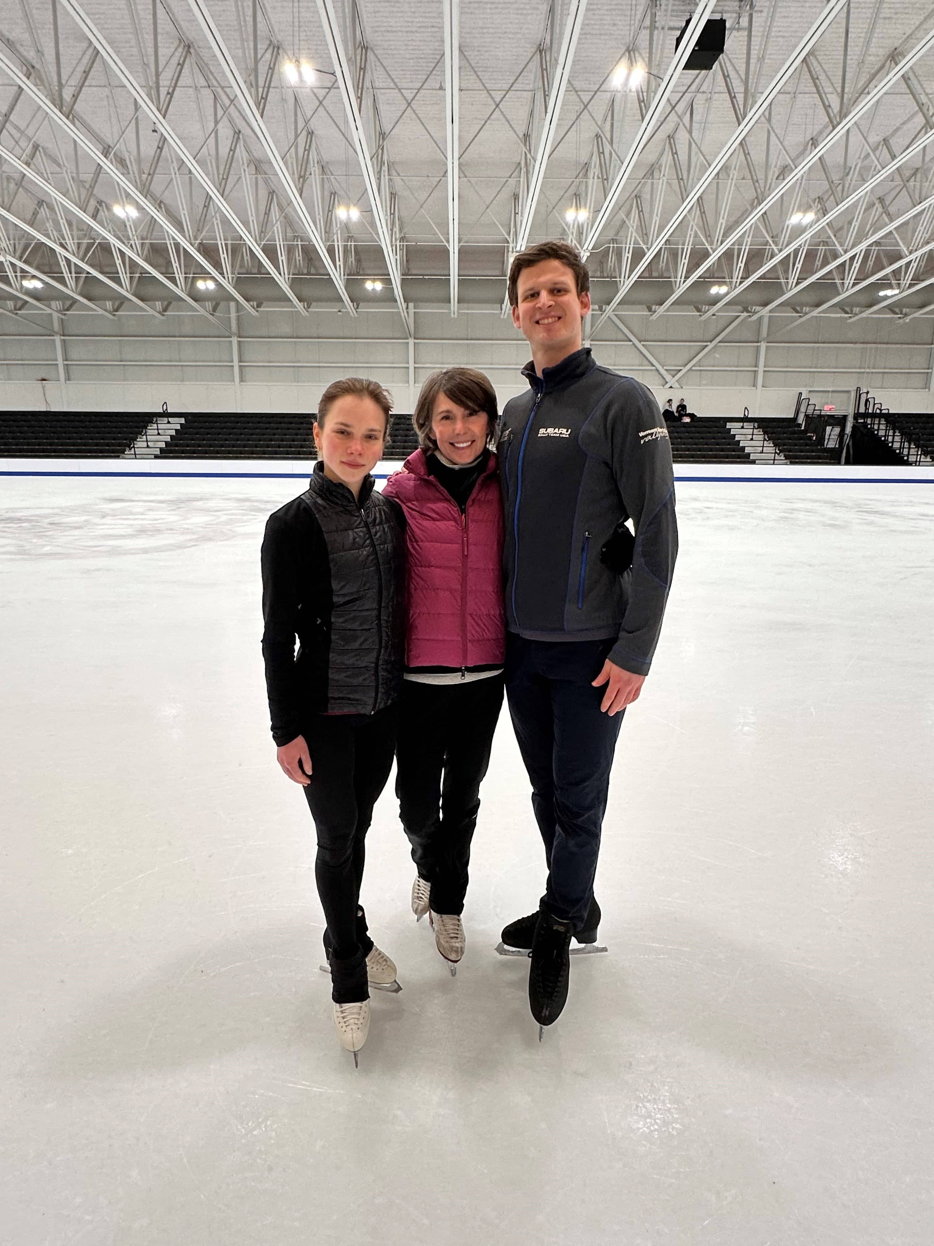 Dressed in black, Alisa Efimova and Misha Mitrofanov with choreographer Renee Roca at center ice at The Skating Club of Boston. 